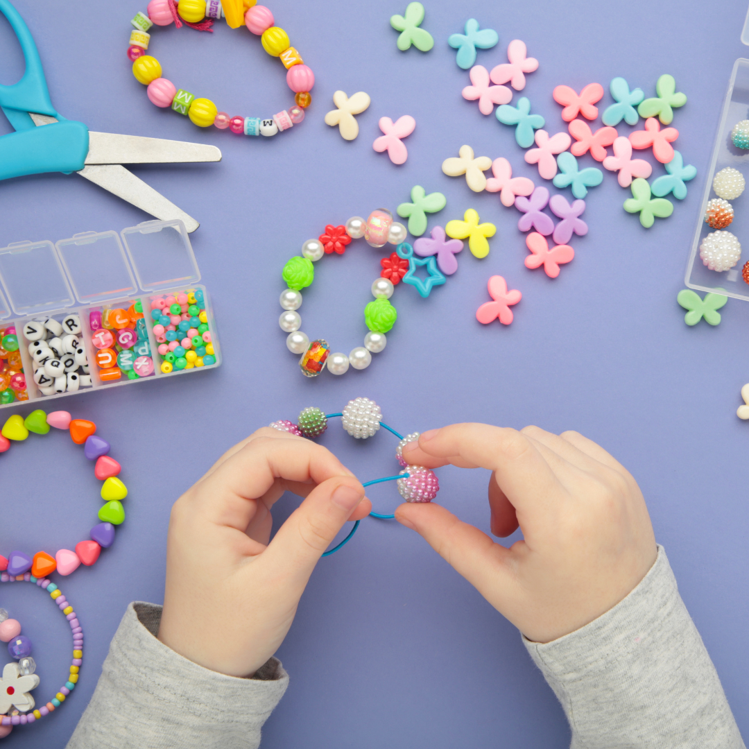 A bird's eye view of a child making a friendship bracelet at a table